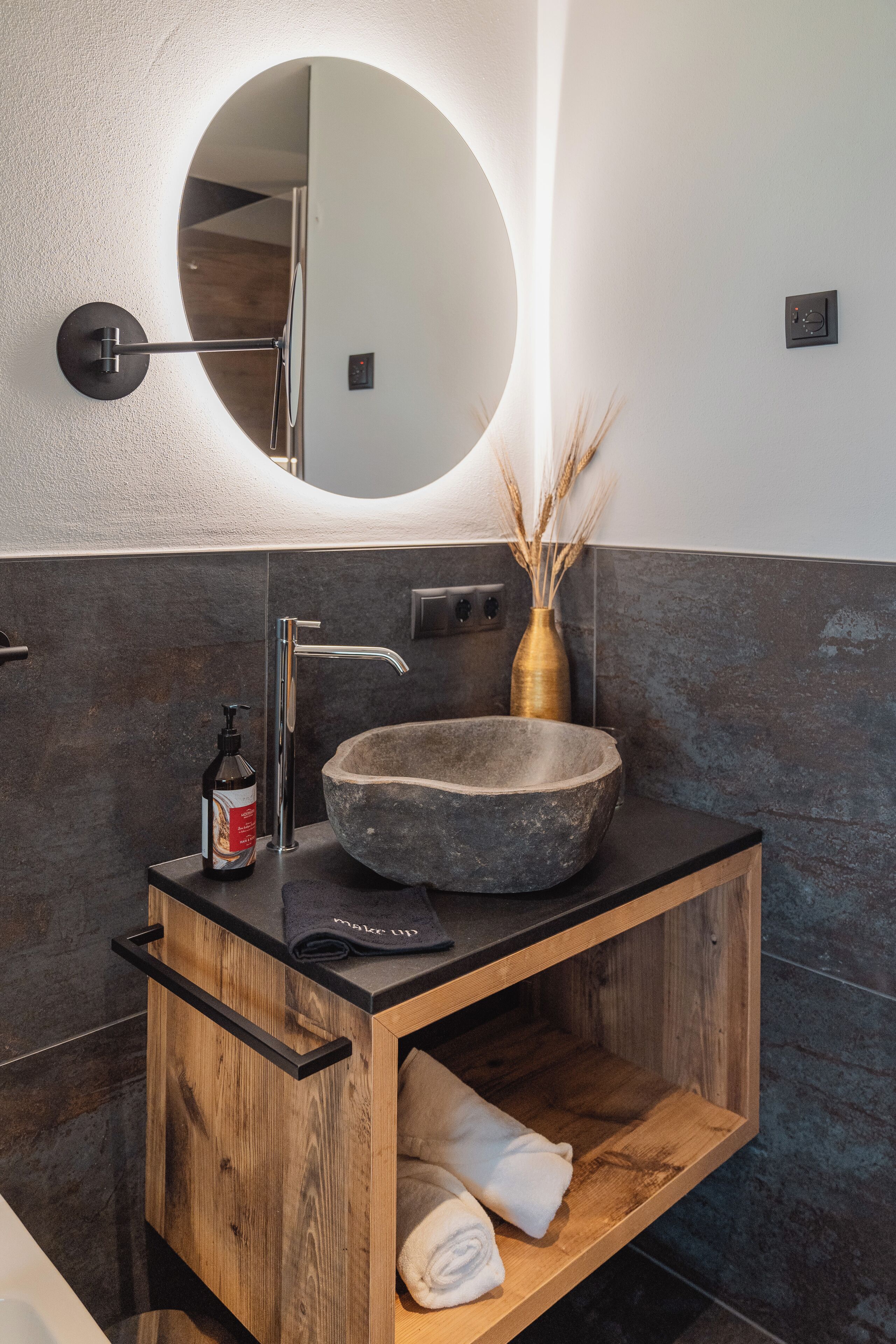 Un bagno moderno con uno specchio rotondo, un lavabo in pietra e un mobile contenitore in legno.