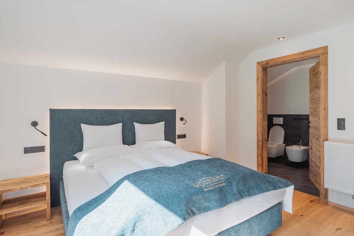 Une chambre à coucher moderne avec un grand lit, une tête de lit en bois et une vue sur la salle de bain.