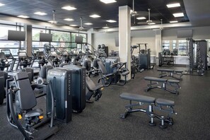 Een sportschool met diverse fitnessapparaten, waaronder loopbanden, krachttoestellen en banken.