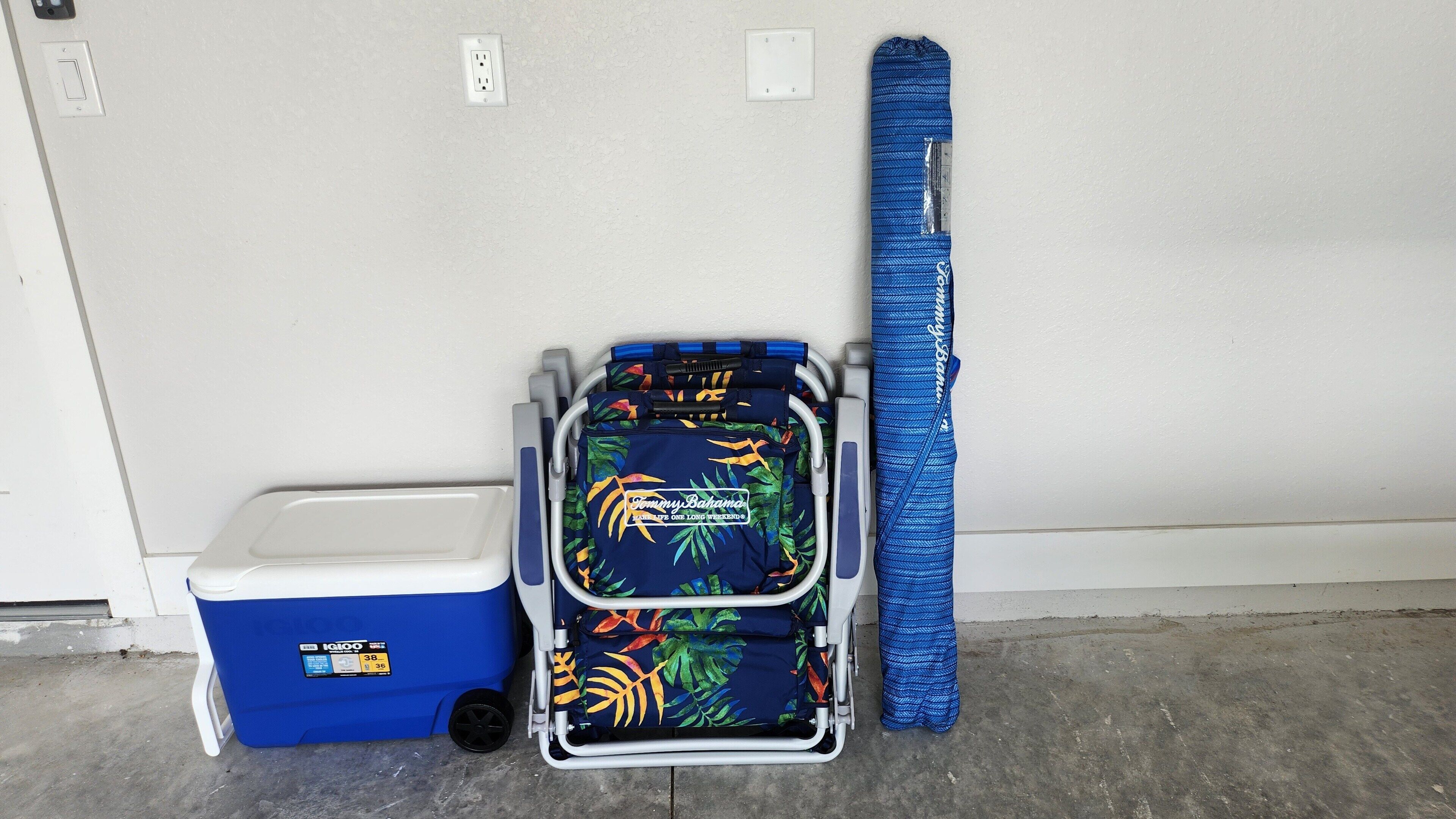A wheelchair, a blue cooler, and a blue towel leaning against a wall.