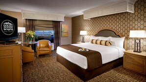 Ein Hotelzimmer mit einem großen Bett, einem Schreibtisch mit Fernseher, einem Sessel und Blick auf die Stadt.