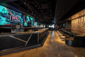 A modern bar area with a large digital screen displaying 'TROY Liquor Bar' and a stone wall on the right. - 1-Bedroom Suite at a 4⭐️ Hotel (Las Vegas)