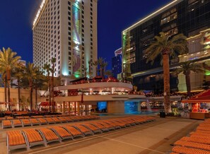 A hotel with a pool area, multiple floors, and a large building in the background.
