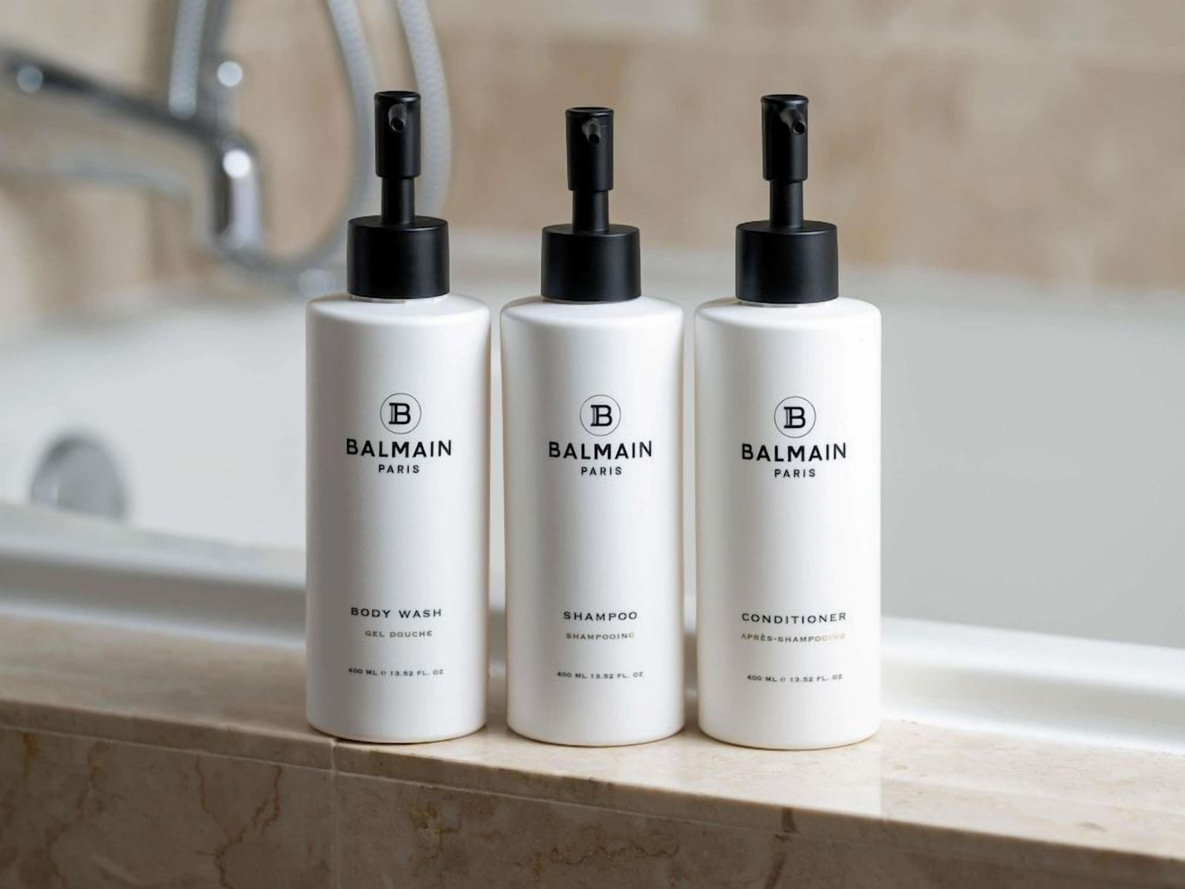 Three bottles of Balmain Paris body wash, shampoo, and conditioner on a bathroom counter.