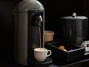 Una máquina de café Nespresso con una taza de café sirviéndose, una jarra de café y una caja de cápsulas de café.