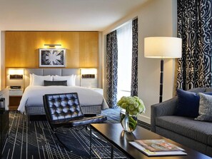 A hotel room with a bed, a seating area with a table, a lamp, and a decorative vase with flowers.