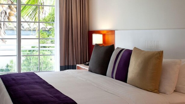 Hotelkamer met een groot bed, nachtkastje met lamp, uitzicht op groen en raam met gordijnen.