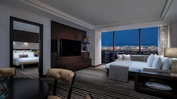 Habitación de hotel con cama, sofá, televisión, mesa de comedor y vista panorámica de la ciudad.