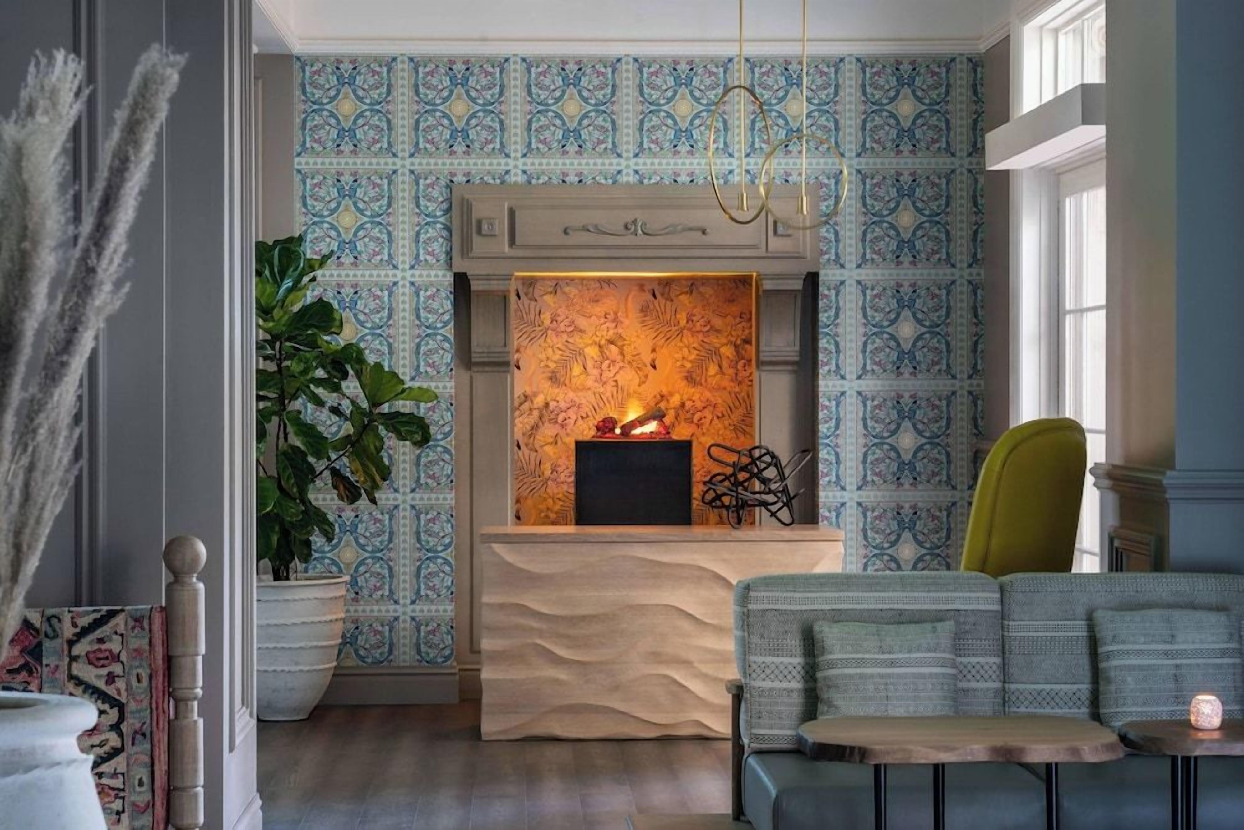 A room with patterned wallpaper, a fireplace with a fire, a sofa, and a chair.