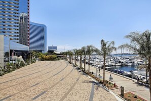 A beachfront promenade with a marina, modern buildings, and palm trees.