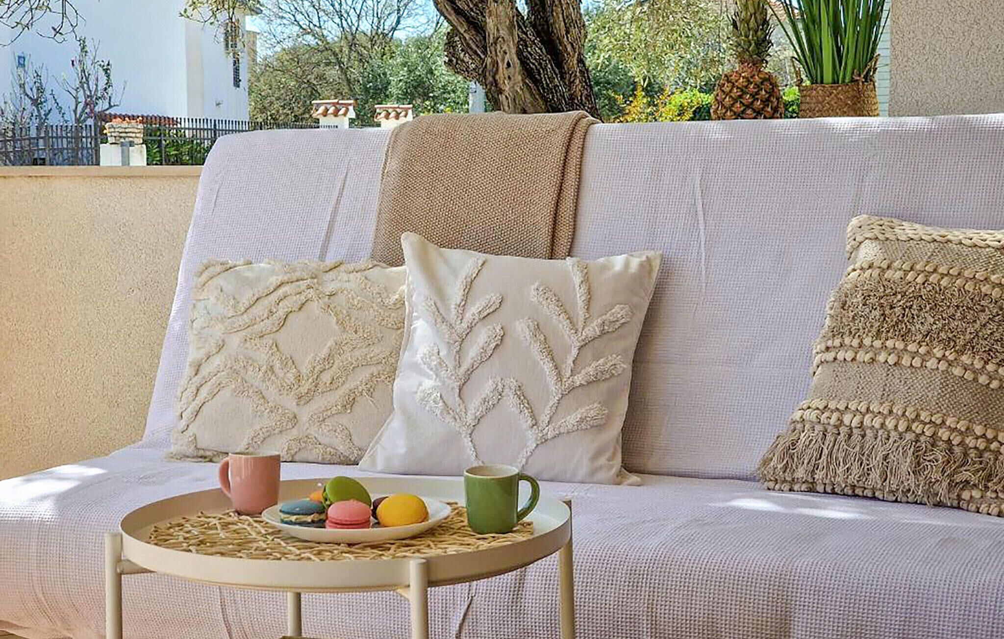 A sofa with decorative pillows, a small table with a placemat, and a plate of colorful macarons.