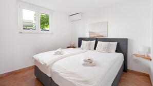 Une chambre avec un lit double, une table de chevet avec une lampe, un climatiseur fixé au mur et une fenêtre donnant sur un paysage verdoyant.