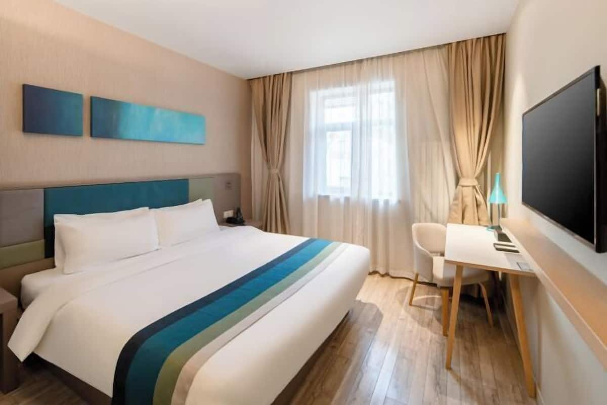 A hotel room with a bed, a desk, a chair, a TV, and curtains.