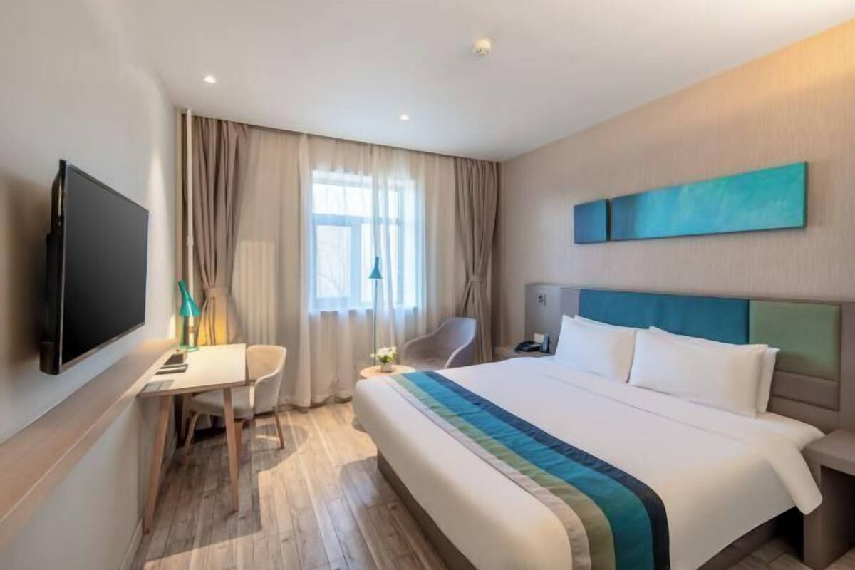 A hotel room with a bed, a desk, a chair, a TV, and a window with curtains.