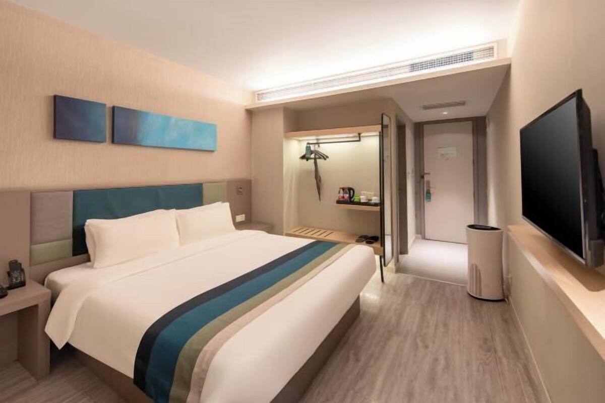 A hotel room with a bed, a TV, a desk, and a bathroom visible through an open door.