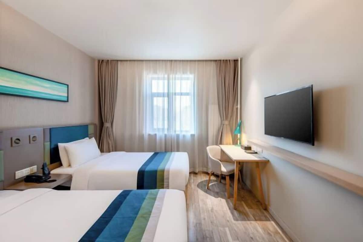 A hotel room with two beds, a desk, a TV, and a window with curtains.