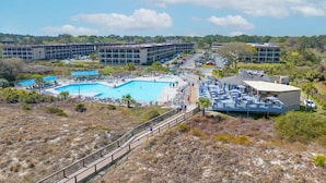 Ein Resort mit mehreren Schwimmbecken, einem überdachten Bereich inklusive Sonnenschirmen und einem großen Gebäude im Hintergrund.