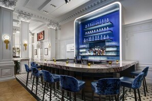 Un espace bar doté d’un comptoir en marbre, de tabourets de bar bleus et d’une étagère bleue rétroéclairée où sont exposées des bouteilles.