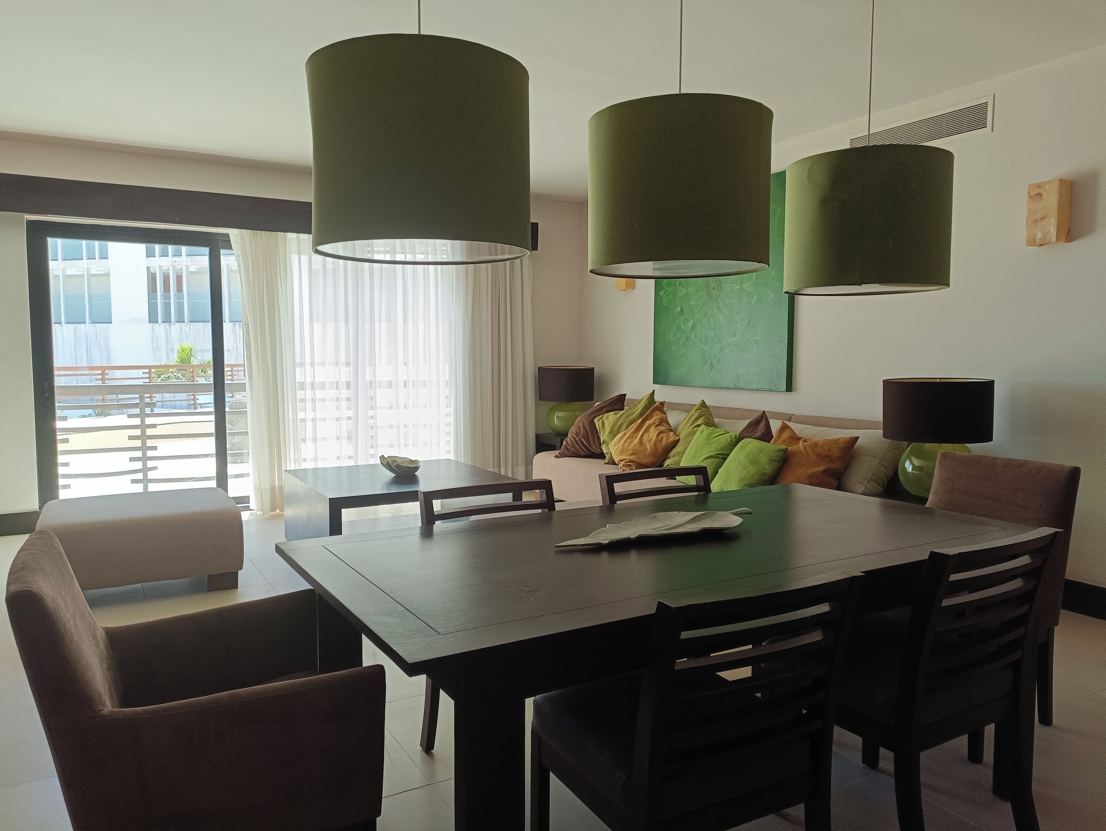 Une chambre d’hôtel moderne dotée d’un coin repas, d’un canapé avec des coussins et d’une grande fenêtre offrant une vue sur la ville.