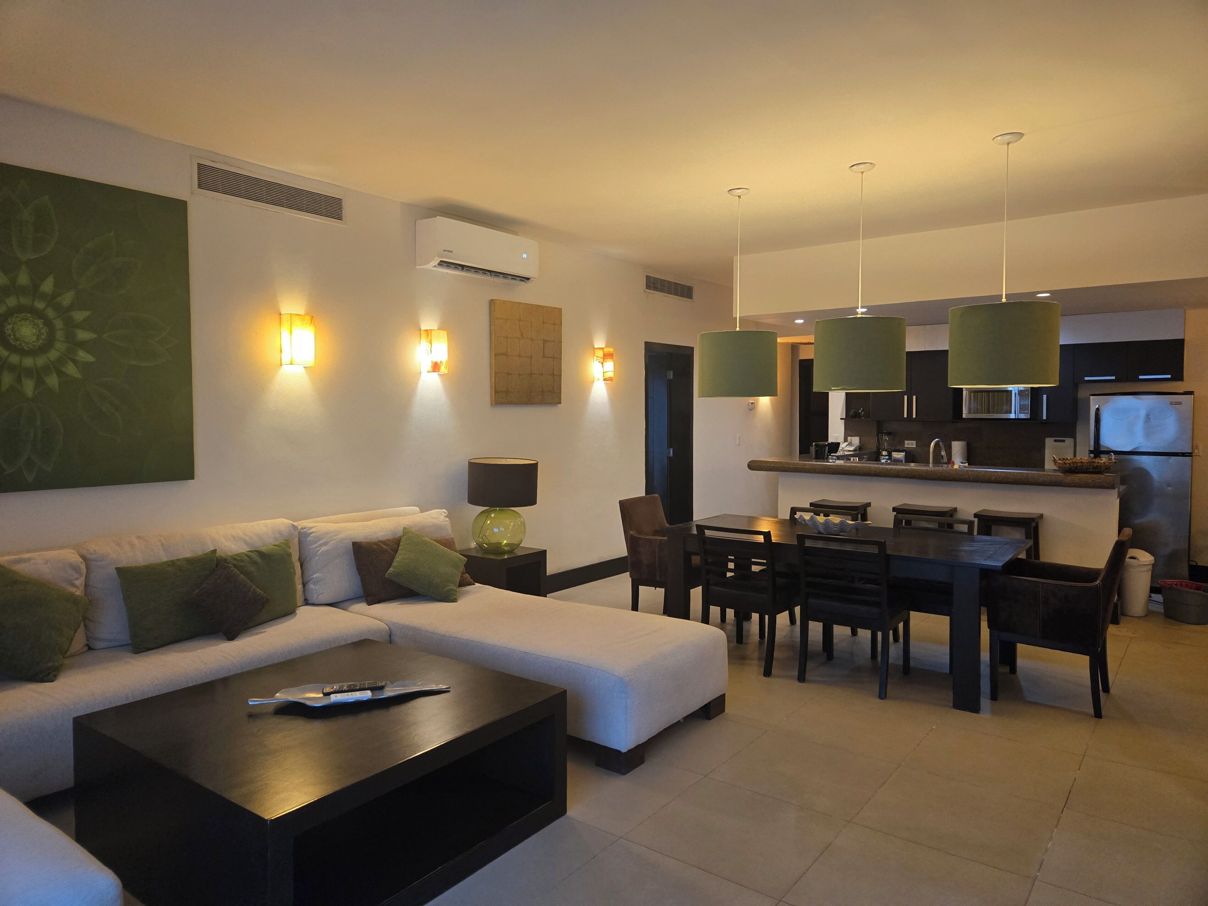 Una sala de estar moderna con un sofá, una mesa de centro y un comedor con sillas, y una cocina al fondo.
