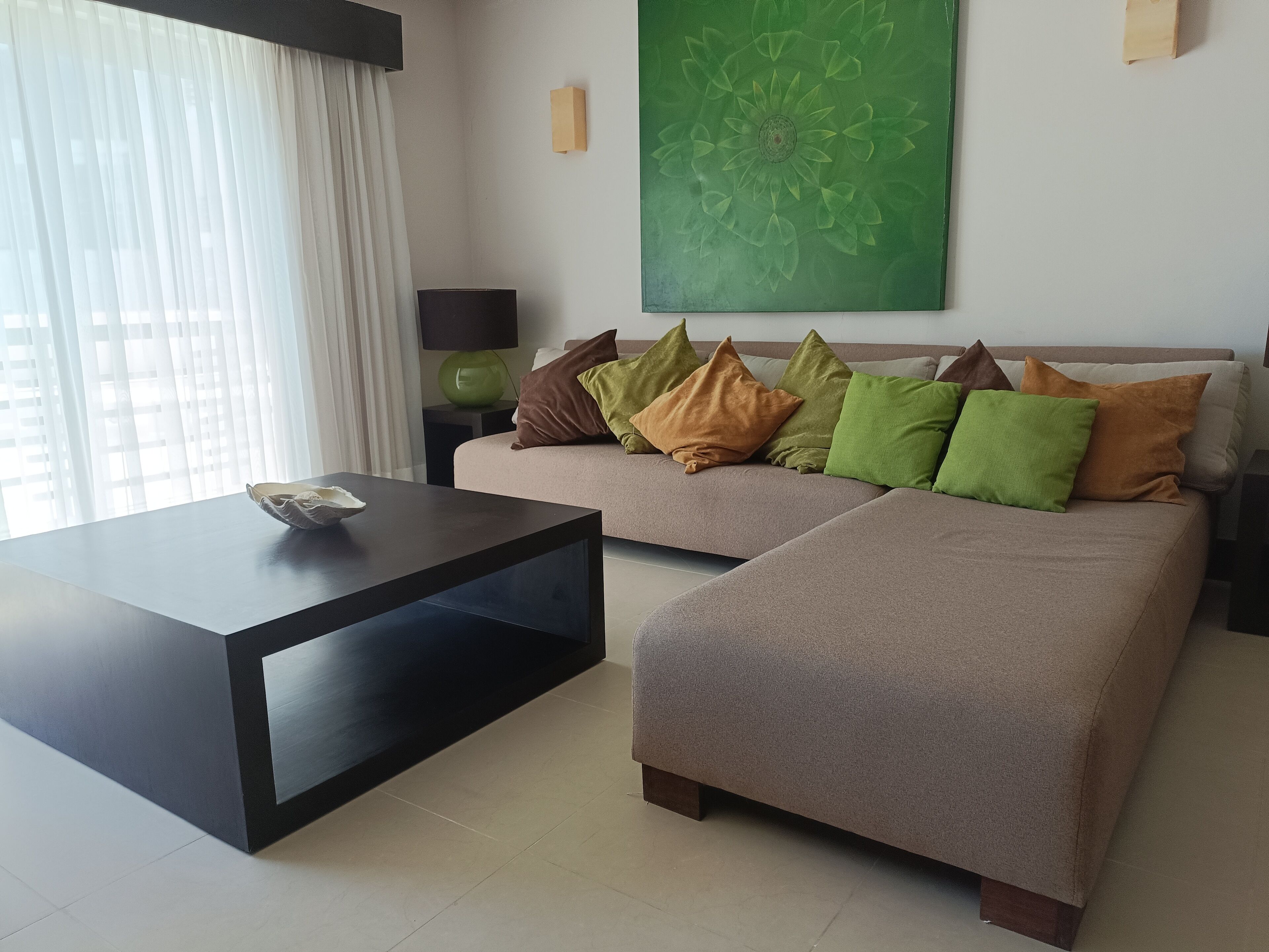 A modern living room with a sofa, a coffee table, and a green abstract painting on the wall.