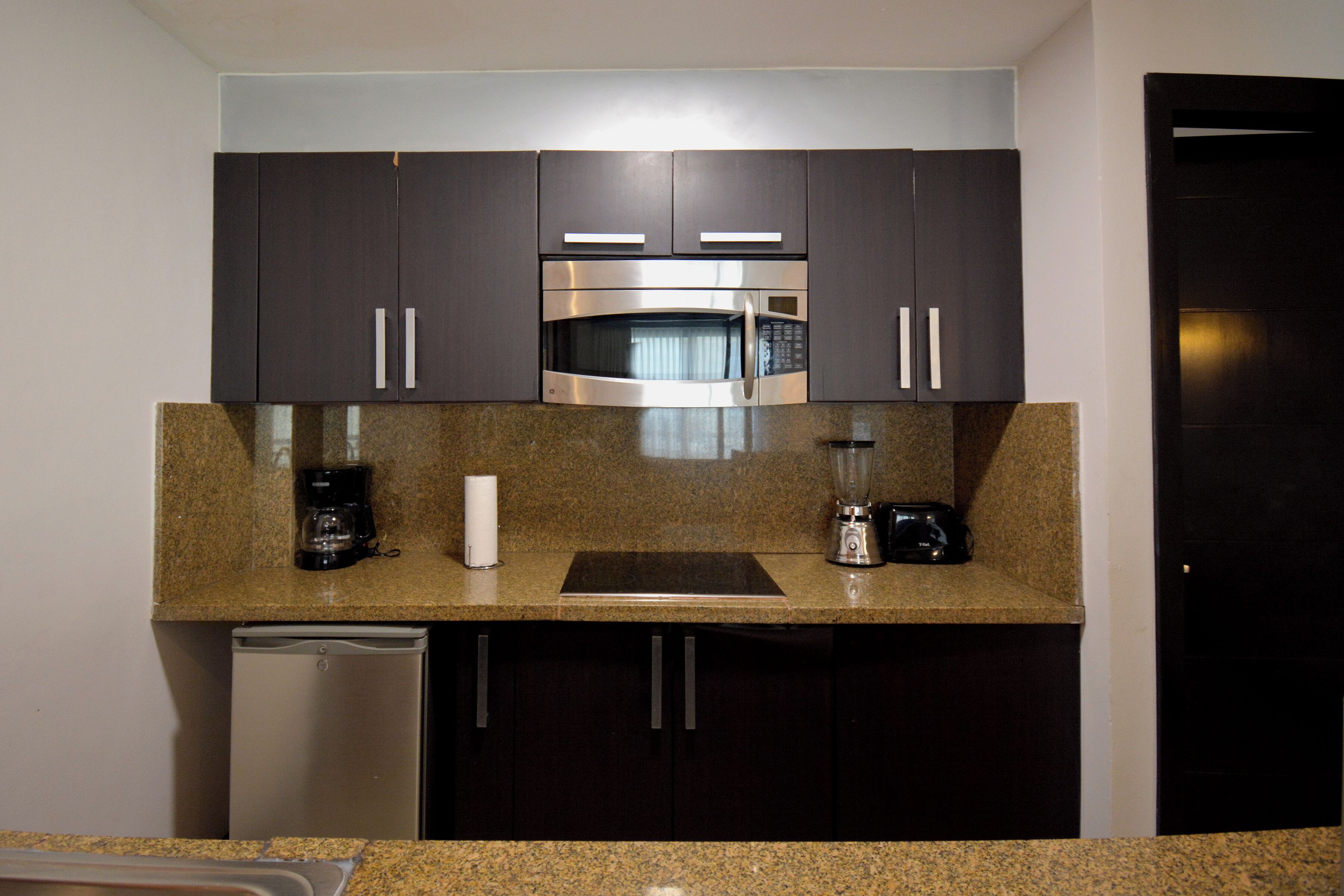 A kitchen with dark cabinets, a stainless steel microwave, a coffee maker, and a blender on the countertop.