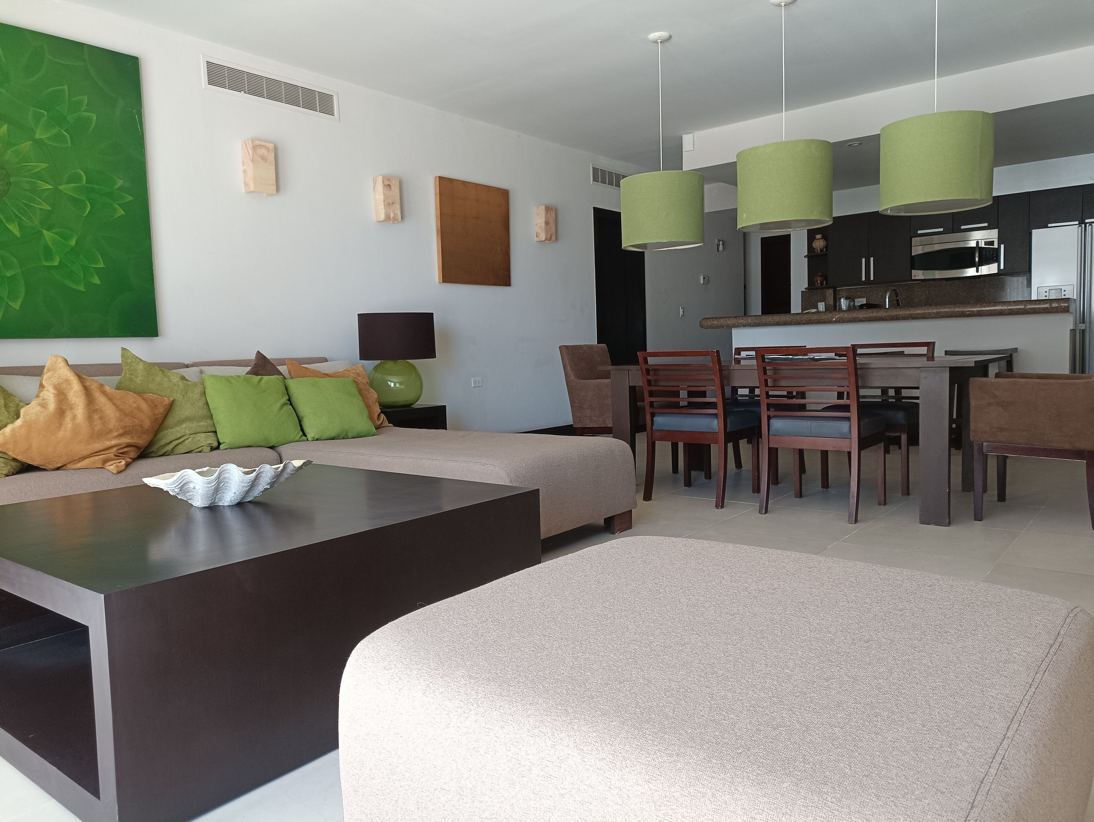 A modern living room with a sofa, coffee table, and dining area with chairs and a kitchen in the background.