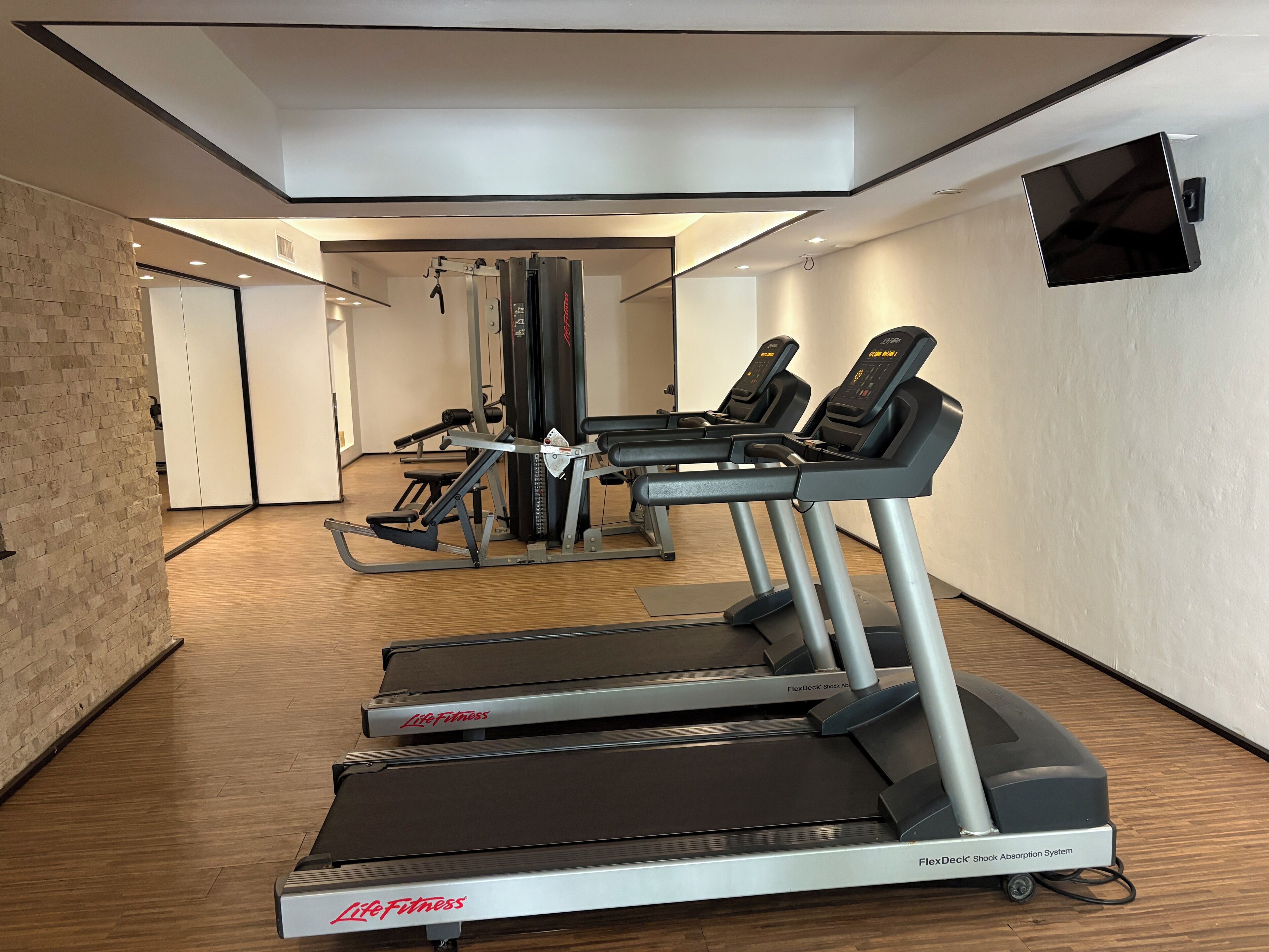 Une salle de sport équipée de tapis de course, d’appareils de musculation et d’un téléviseur fixé au mur.