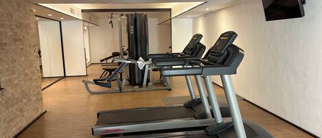 Une salle de sport équipée de tapis de course, d’appareils de musculation et d’un téléviseur fixé au mur.