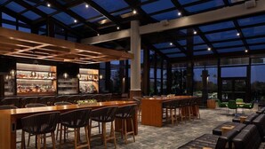 A modern bar area with wooden bar counters, bar stools, and a seating area with sofas and chairs.