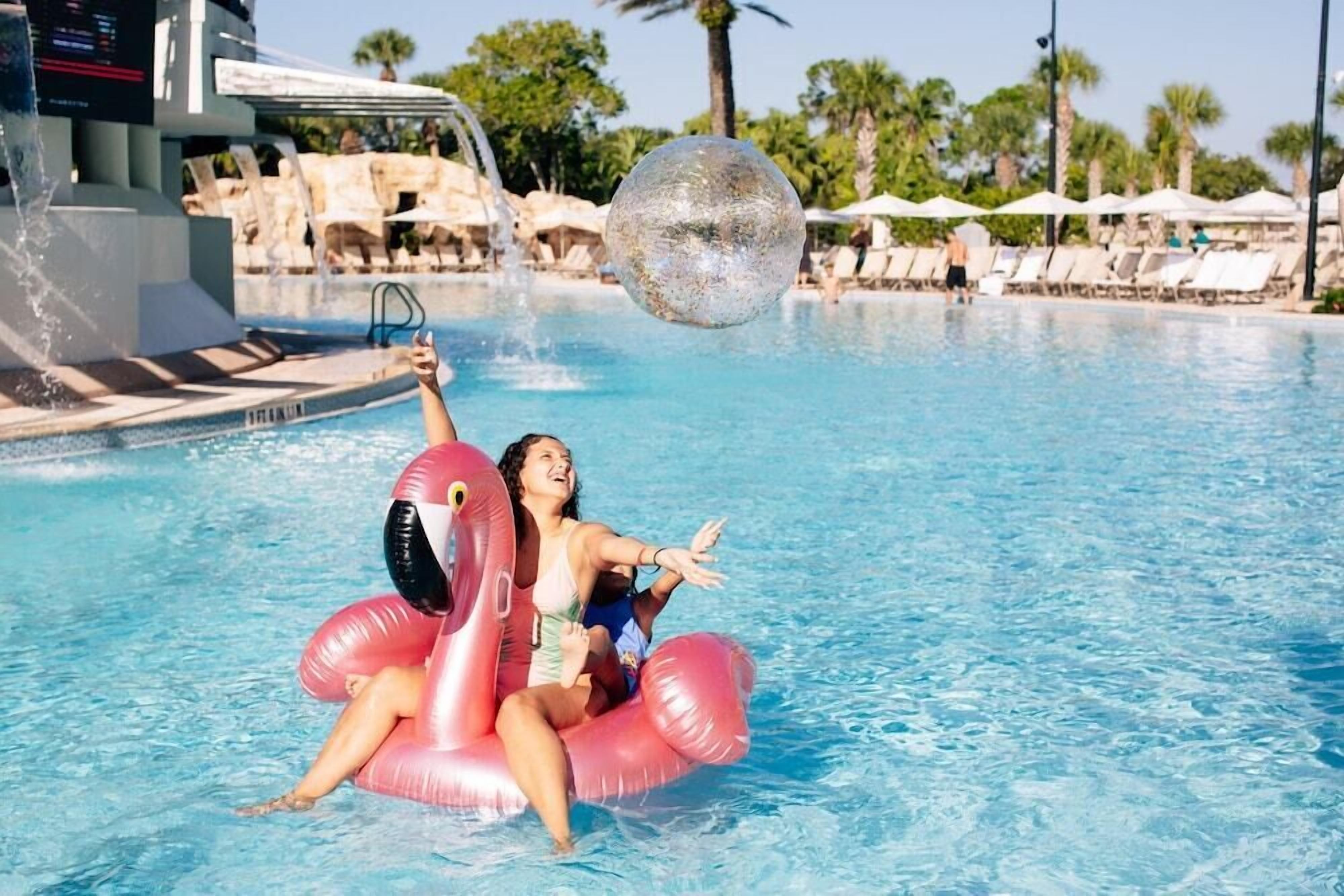 Een zwembad met ligbedden en parasols, een waterpartij en een grote opblaasbare bal.