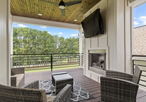 A covered outdoor area with wicker furniture, a fireplace, and a view of trees.