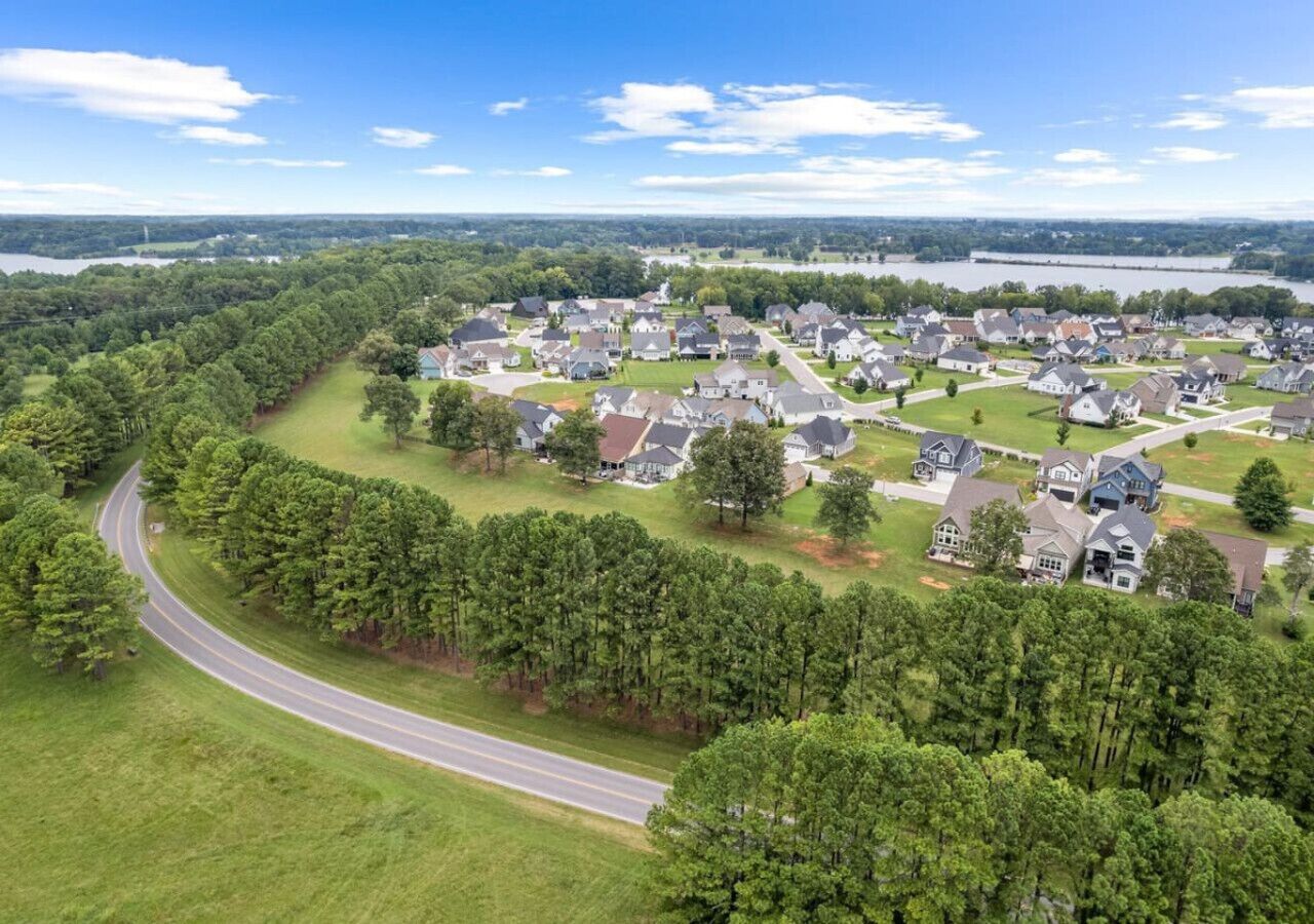 Luchtbeeld van een woongebied met huizen, een bochtige weg en een meer op de achtergrond.