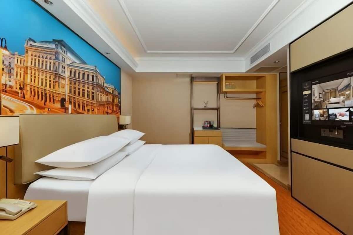 A hotel room with a bed, a desk, a mirror, a wardrobe, and a wall-mounted TV.