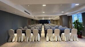 Een congreszaal met rijen tafels en stoelen, een podium aan de voorzijde en een groot raam aan de rechterkant.
