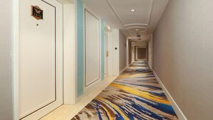 Een hotelgang met een kamerbreed tapijt, witte deuren en een plafond met ingebouwde verlichting.