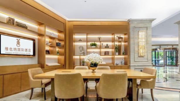 Een moderne hotellobby met een lange receptiebalie, comfortabele zitplaatsen en een decoratieve wand met planken.
