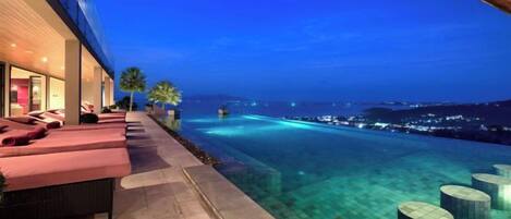 A poolside area with lounge chairs and a clear view of the ocean at dusk.