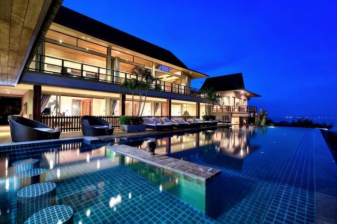 Un hôtel moderne doté d’une grande piscine à débordement, d’un balcon au deuxième étage et offrant une vue sur l’océan au crépuscule.