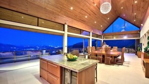 Cozinha moderna com ilha grande, armários de madeira e vista da cidade ao entardecer.
