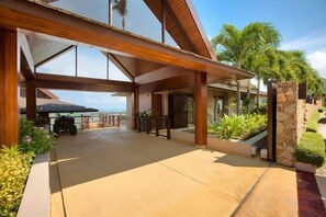 Un espacio al aire libre techado con piso de concreto, palmeras y un muro de piedra.