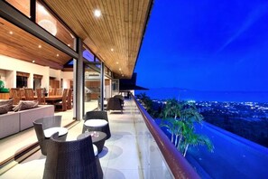 A balcony with outdoor seating, a view of the city, and a wooden ceiling. - Baan Grand Vista - Panoramic Sea View (Koh Samui)
