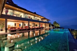 A modern hotel with a pool, outdoor seating, and a view of the sea. - Baan Grand Vista - Panoramic Sea View (Koh Samui)