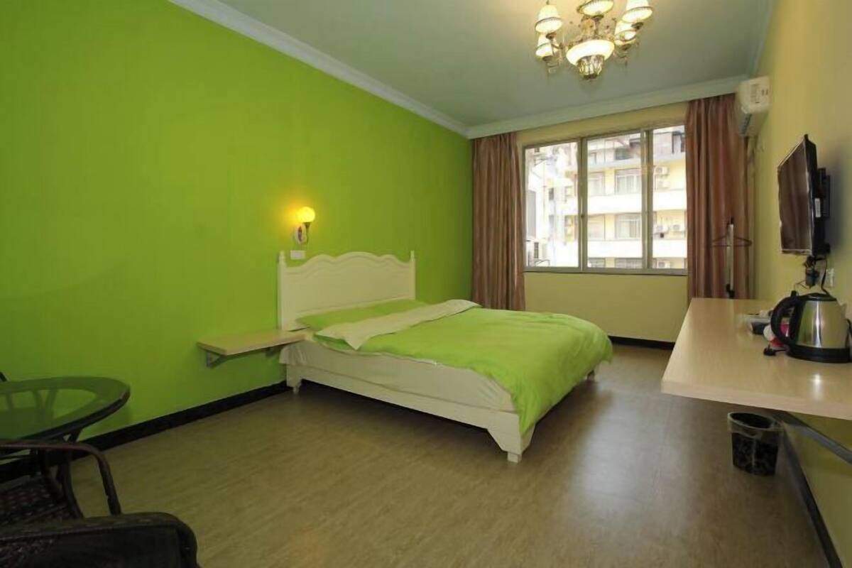 A room with a bed, a table, a chair, a window with curtains, and a television.