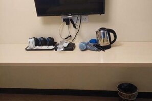 Un televisor de pantalla plana montado en la pared, una cafetera, un juego de teteras, un secador de pelo y un cubo de basura.