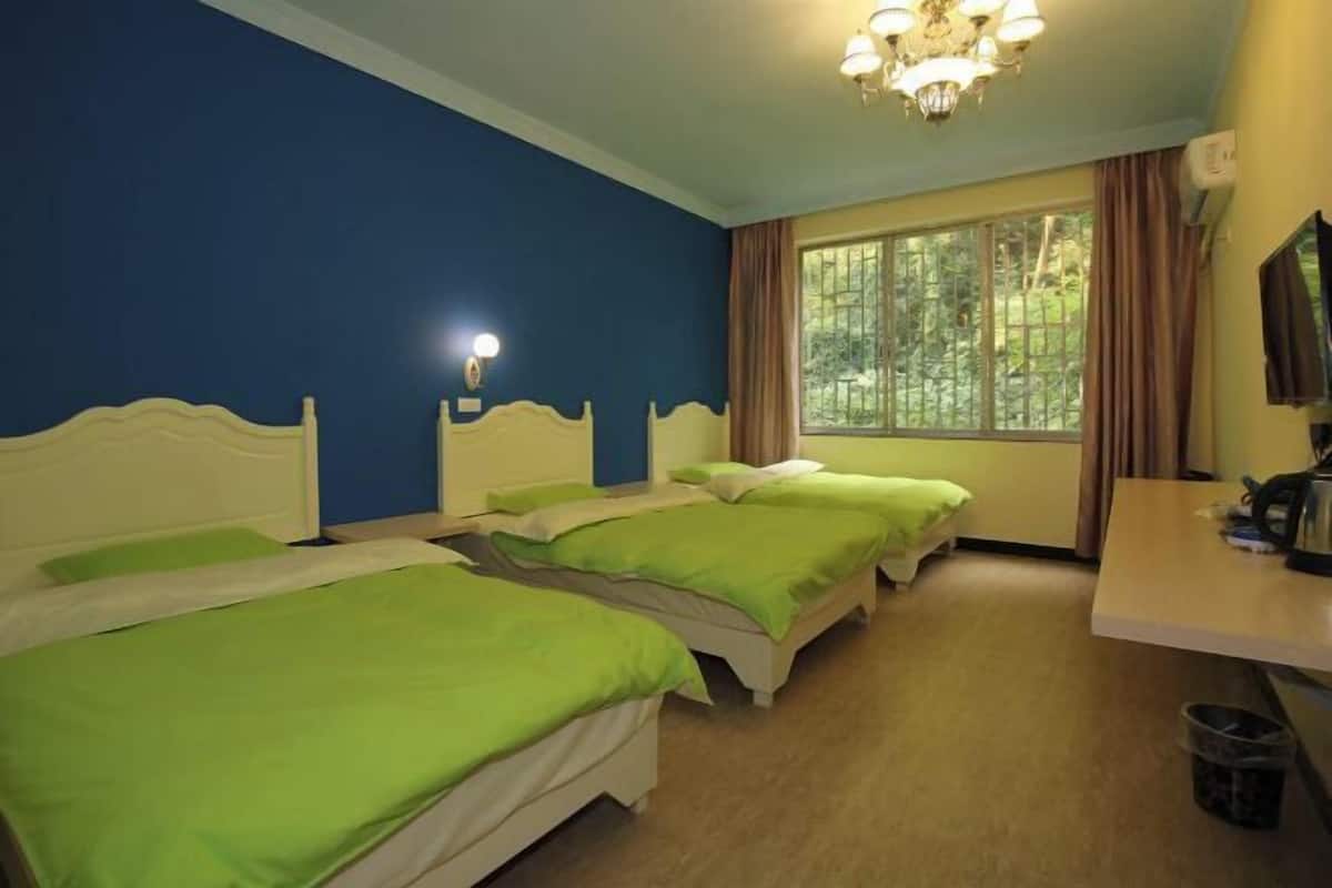A room with three beds, a desk, a chandelier, and a window with curtains.