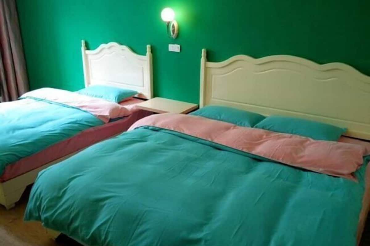 A room with two beds, each with a white headboard, and a green wall.