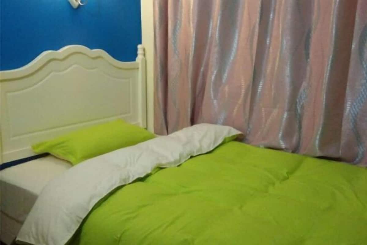 A bed with green bedding, a white headboard, and a blue wall.