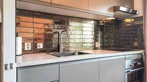 Een moderne keuken met een RVS-gootsteen, een afzuigkap en een betegelde spatwand.