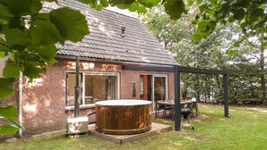 Een huis met een bakstenen gevel, een houten jacuzzi en een terras met tuinmeubilair.